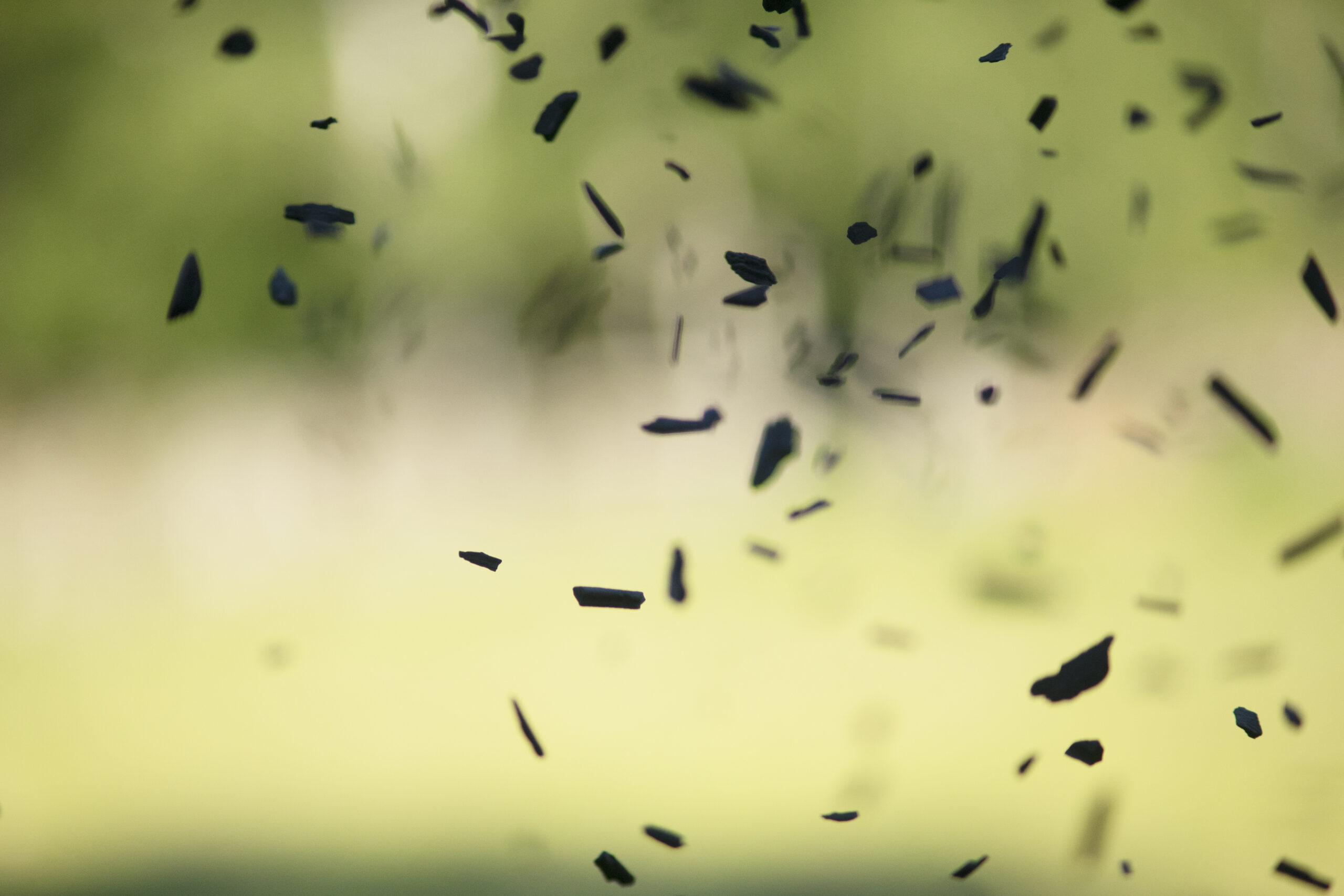 Biokolbitar som faller i luften med suddig grönska i bakgrunden