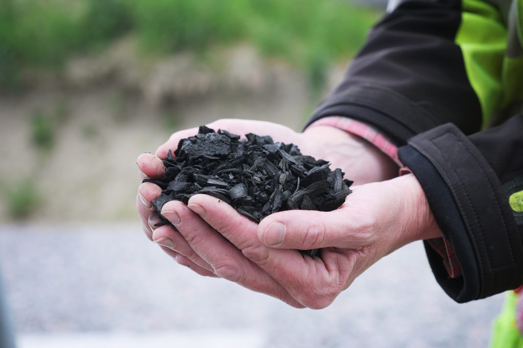 Bild på händer som håller biokol framför en suddig grön utomhusmiljö.