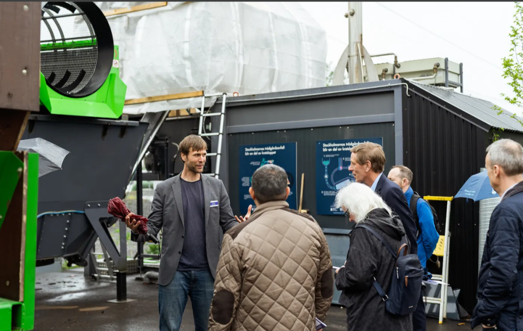 Mattias står framför biokolpannan och talar med åhörare inom projektet Stockholm Biochar Project